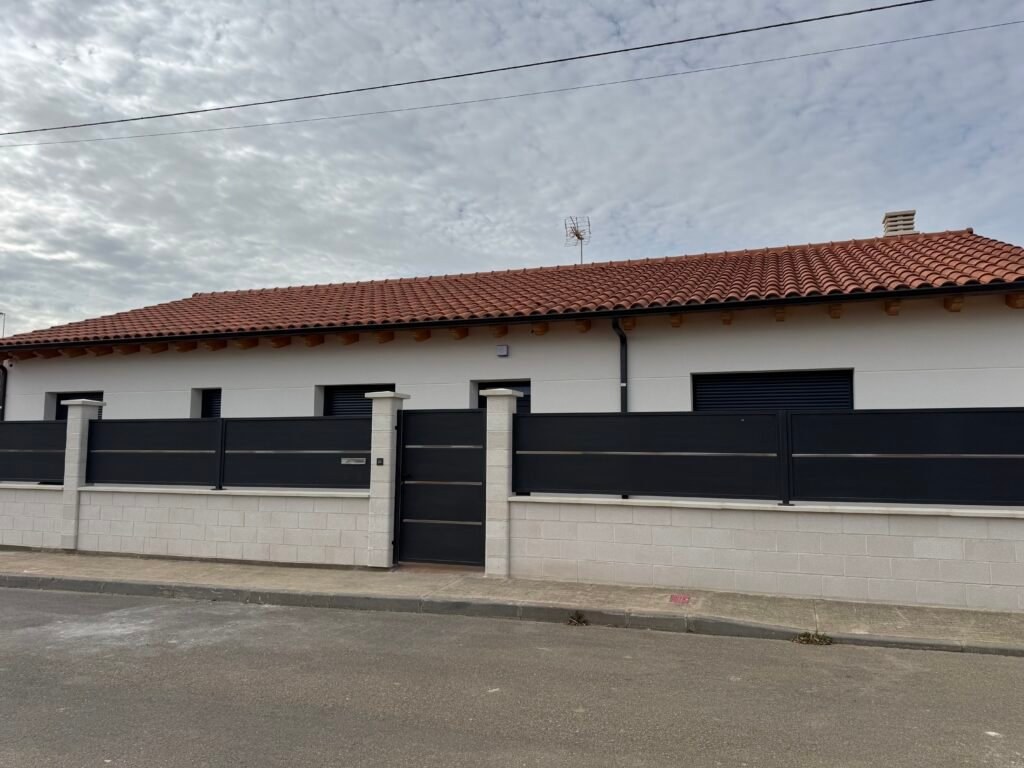Fachada principal de vivienda unifamiliar en Villar del Yermo (León) Fachada principal de vivienda unifamiliar con cerramiento metálico y cubierta de teja en Villar del Yermo, León